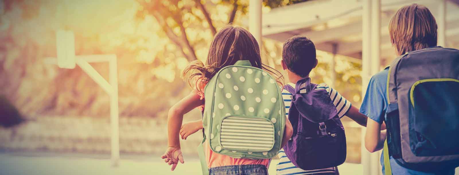 Children with backpacks running towards a playground