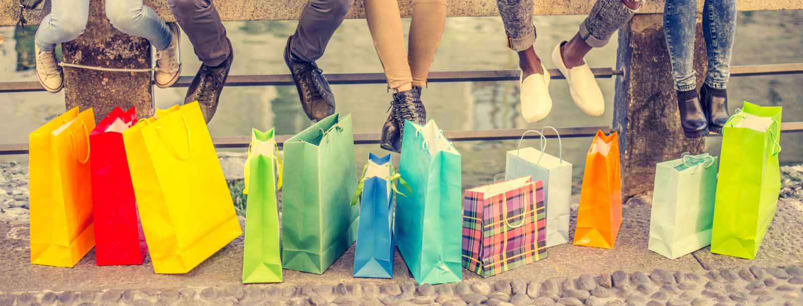 Shopping bags sitting on the ground next to guardrail with people sitting on it